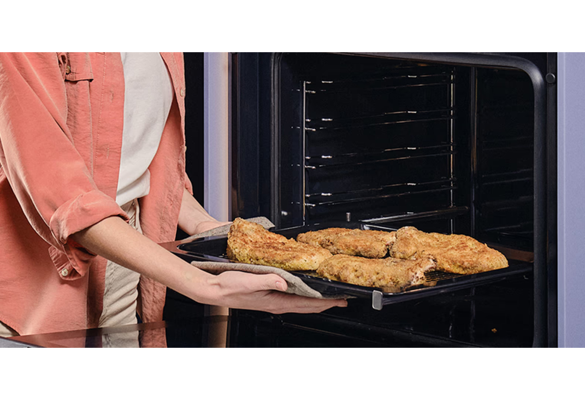 Απεικονίζεται γυναίκα να βγάζει ταψί με κρέας από τον φούρνο.